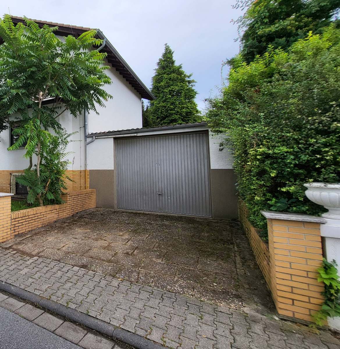 Zweite Garage als Anbau am Haus, graues Schwingtor, davor ein gepflasterter Stellplatz mit eigener Zufahrt von der Straße